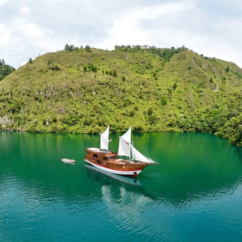 Kapal Phinisi tradisional berlayar di perairan jernih Labuan Bajo dengan latar Pulau Komodo