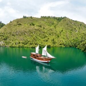 Kapal Phinisi tradisional berlayar di perairan jernih Labuan Bajo dengan latar Pulau Komodo