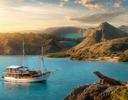Traditional phinisi boat sailing through turquoise waters during a Komodo boat tour, with a Komodo dragon and Flores volcanic hills in the background