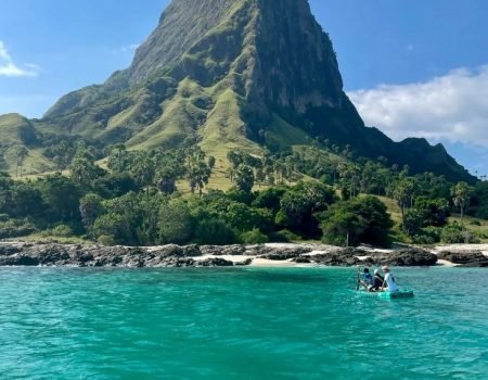 Scenic beach view of Mules Island with clear turquoise water and lush green hills.