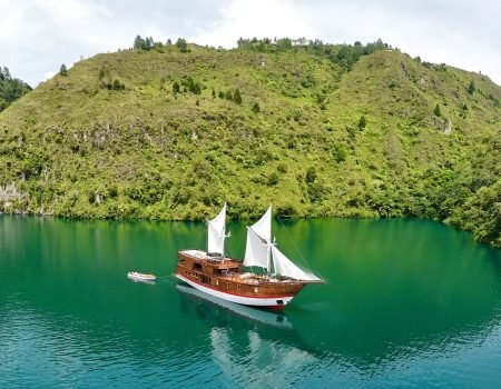 Kapal Phinisi tradisional berlayar di perairan jernih Labuan Bajo dengan latar Pulau Komodo